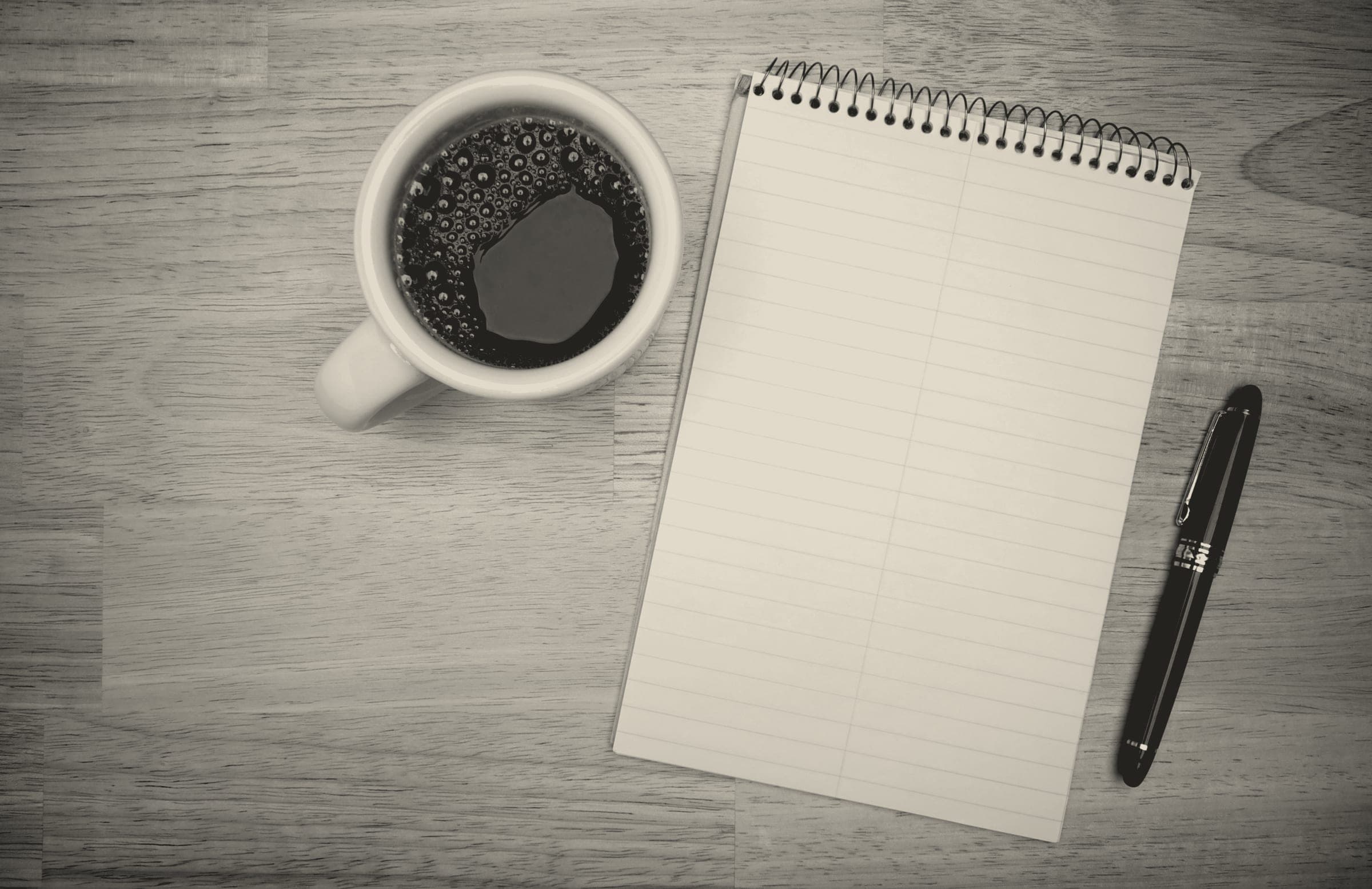 A blank notepad, a pen and a cup of coffee on a desk