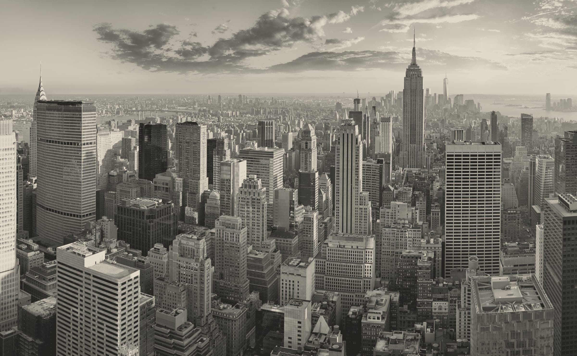 A high-vantage monochrome panorama of Midtown Manhattan looking south, with the Empire State Building rising at centre-right and the Chrysler Building spire visible at far left. Dense clusters of mid-