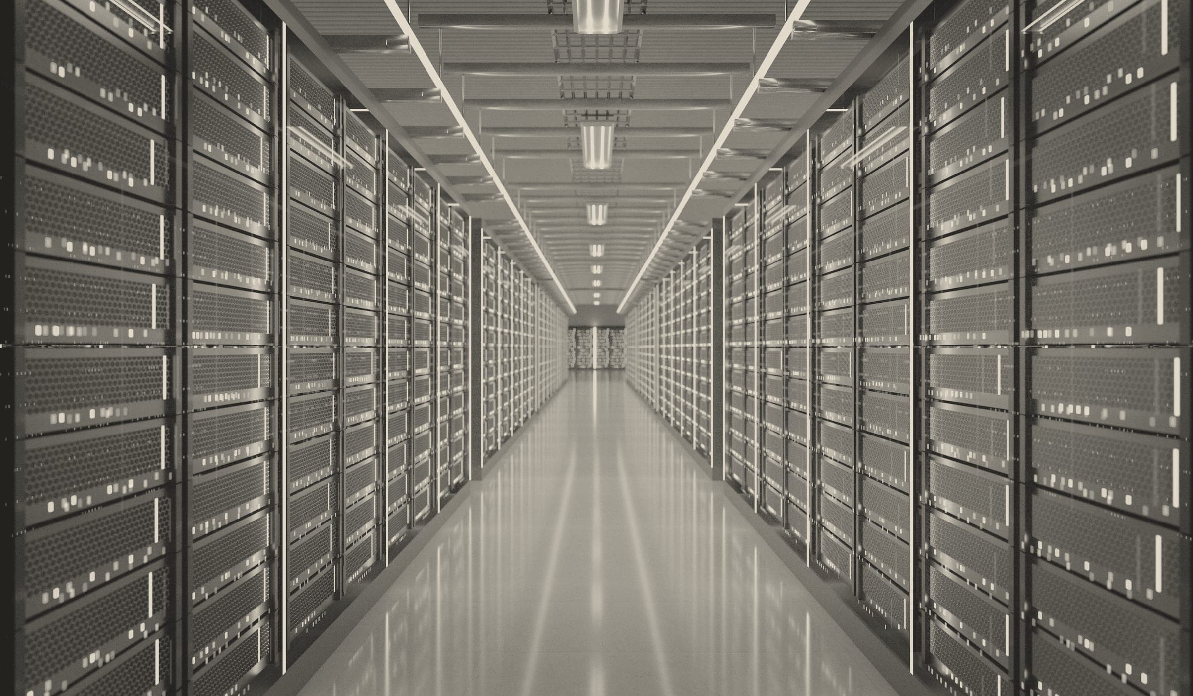 A long, symmetrical corridor inside a data centre, flanked on both sides by towering rows of perforated server racks studded with small indicator lights. Overhead strip lighting and suspended ceiling